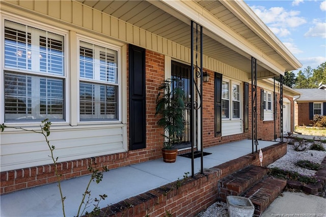 entrance to property with a garage, brick siding, and covered porch