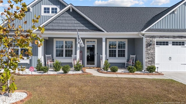 view of front of home with stone siding, a porch, board and batten siding, an attached garage, and a shingled roof