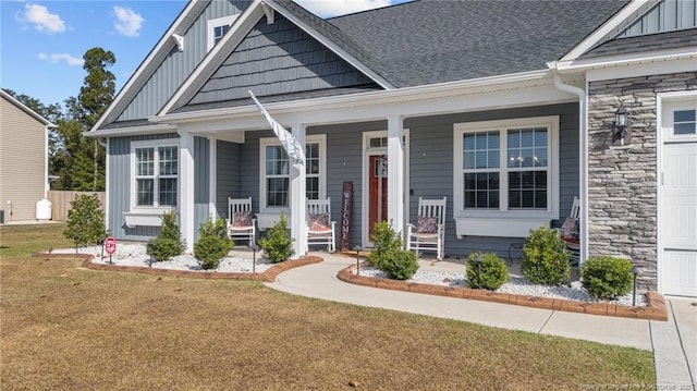 view of front of house with a front lawn, stone siding, covered porch, board and batten siding, and roof with shingles