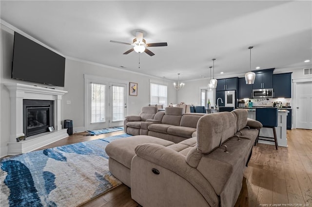 living area featuring a glass covered fireplace, ceiling fan with notable chandelier, wood finished floors, and ornamental molding