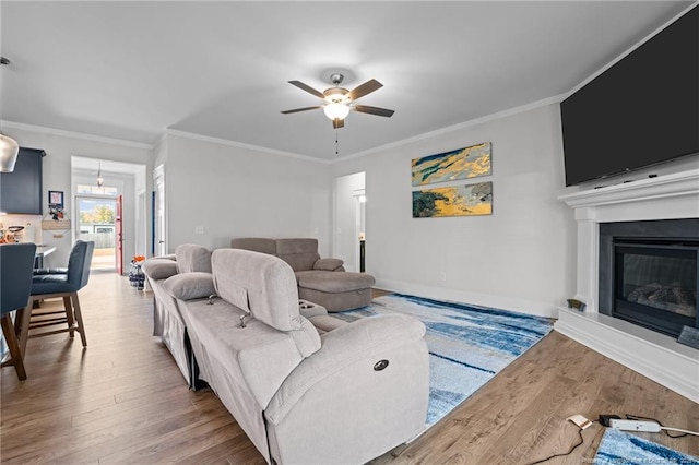 living area featuring a glass covered fireplace, wood finished floors, a ceiling fan, and ornamental molding