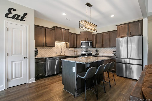 kitchen featuring dark brown cabinetry, dark wood finished floors, light stone counters, stainless steel appliances, and a sink