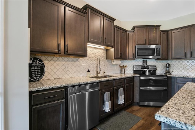 kitchen featuring a sink, light stone counters, dark brown cabinetry, and appliances with stainless steel finishes