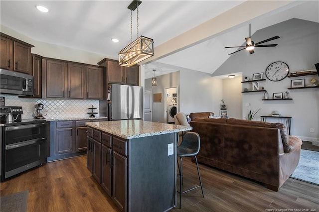 kitchen featuring dark brown cabinets, open floor plan, lofted ceiling with beams, light stone counters, and appliances with stainless steel finishes