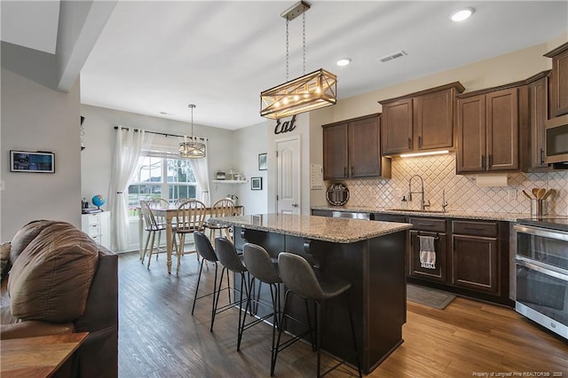 kitchen featuring light stone counters, visible vents, a sink, stainless steel appliances, and a center island