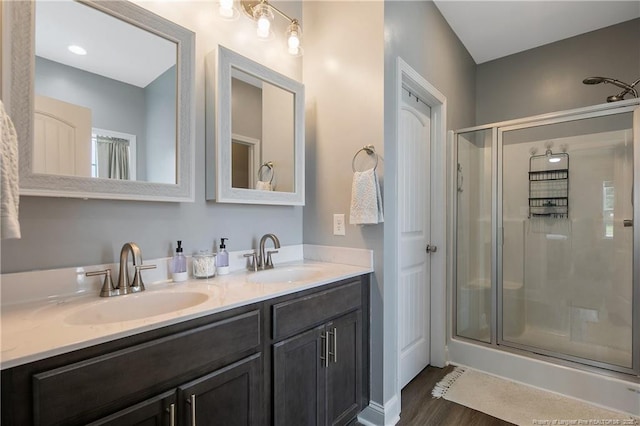 bathroom with a sink, wood finished floors, a stall shower, and double vanity