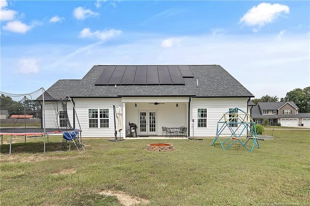 rear view of house featuring a ceiling fan, a trampoline, french doors, a fire pit, and solar panels