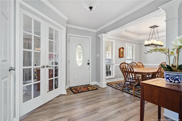 entrance foyer with light wood-type flooring, a tray ceiling, french doors, crown molding, and ornate columns