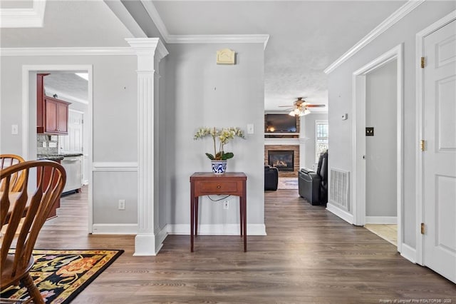 corridor featuring visible vents, wood finished floors, crown molding, and ornate columns