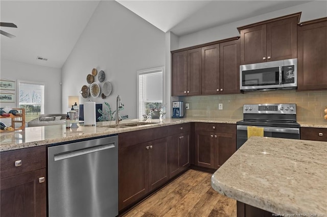 kitchen featuring vaulted ceiling, dark brown cabinets, appliances with stainless steel finishes, and a sink