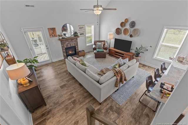 living area with a brick fireplace, wood finished floors, visible vents, and ceiling fan