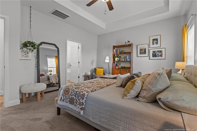 bedroom with a tray ceiling, carpet flooring, baseboards, and visible vents