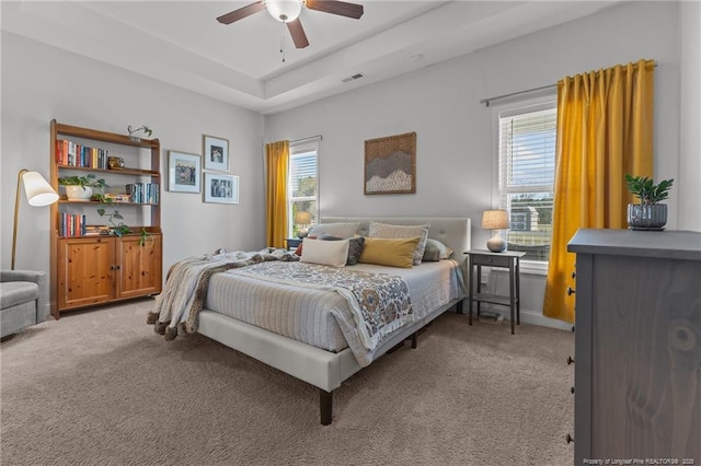 bedroom featuring ceiling fan, a tray ceiling, visible vents, and light carpet