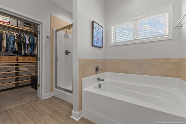 bathroom with a walk in closet, a shower stall, and a garden tub