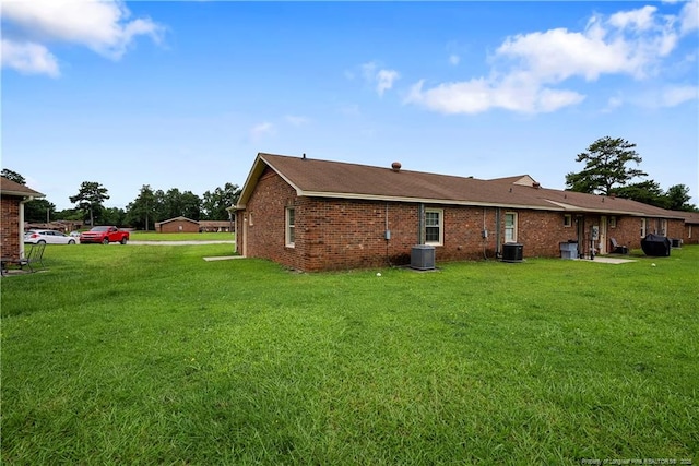 back of property with cooling unit, a lawn, and brick siding