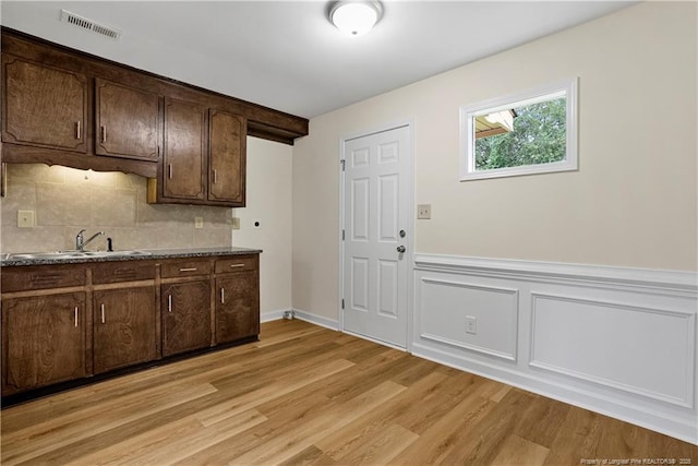 kitchen with a sink, light wood-type flooring, dark brown cabinetry, and backsplash