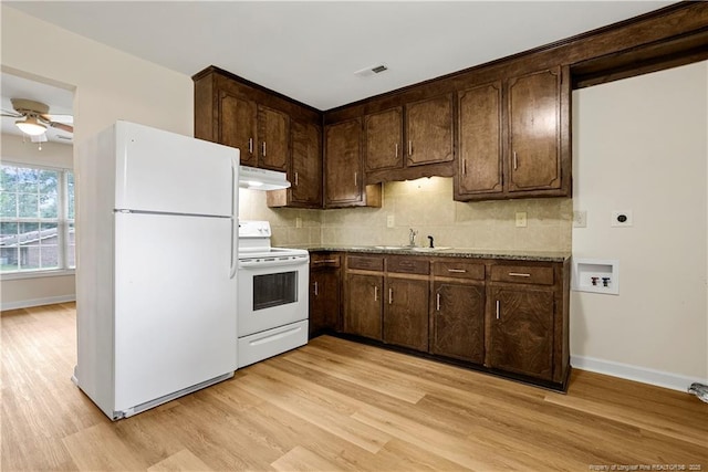 kitchen with white appliances, dark brown cabinetry, light wood-style floors, under cabinet range hood, and tasteful backsplash