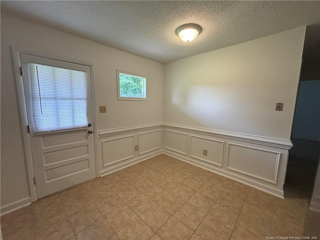 interior space featuring a wainscoted wall, a textured ceiling, and a decorative wall