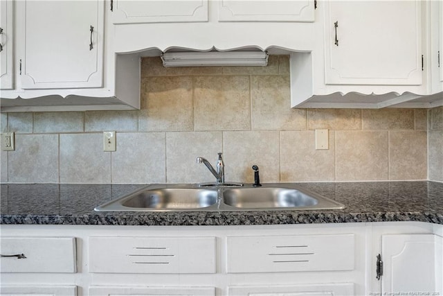 kitchen featuring a sink, tasteful backsplash, dark countertops, and white cabinetry