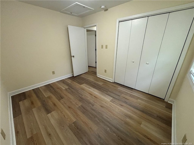 unfurnished bedroom with a closet, baseboards, attic access, and wood finished floors