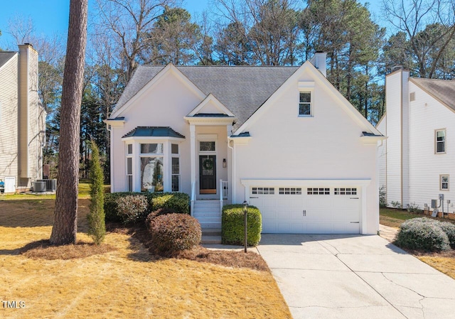 view of front of house featuring central air condition unit, roof with shingles, concrete driveway, a garage, and a chimney