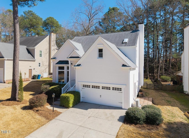 view of front facade featuring fence, roof with shingles, driveway, a chimney, and a garage