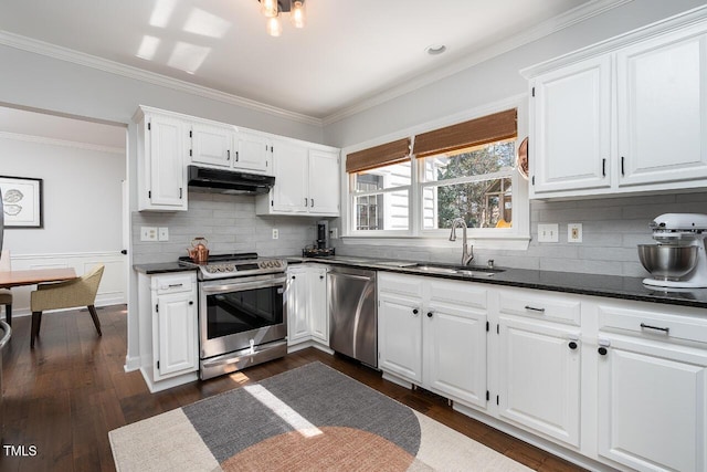 kitchen with a sink, under cabinet range hood, stainless steel appliances, white cabinetry, and dark wood-style flooring