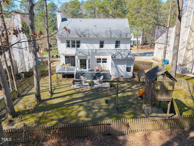 back of property featuring a shingled roof, a wooden deck, a lawn, a chimney, and a fenced backyard