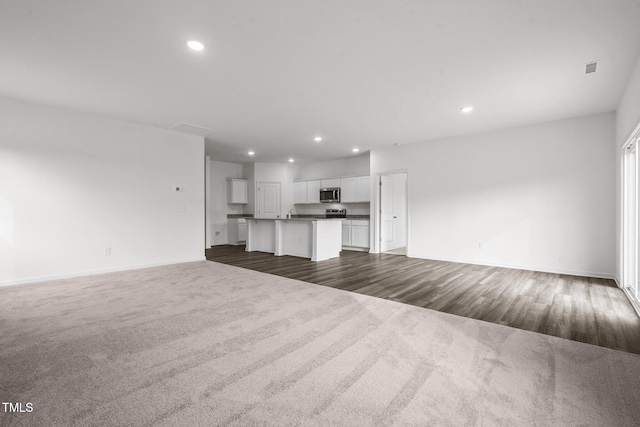 unfurnished living room with dark wood-style floors, recessed lighting, dark colored carpet, and baseboards