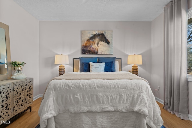 bedroom with baseboards, a textured ceiling, and wood finished floors