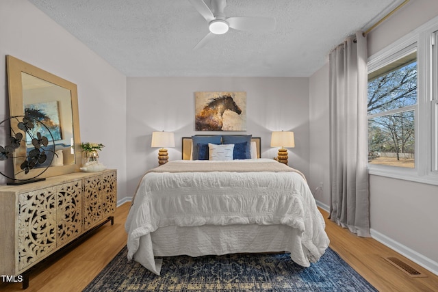 bedroom with visible vents, a textured ceiling, wood finished floors, baseboards, and ceiling fan