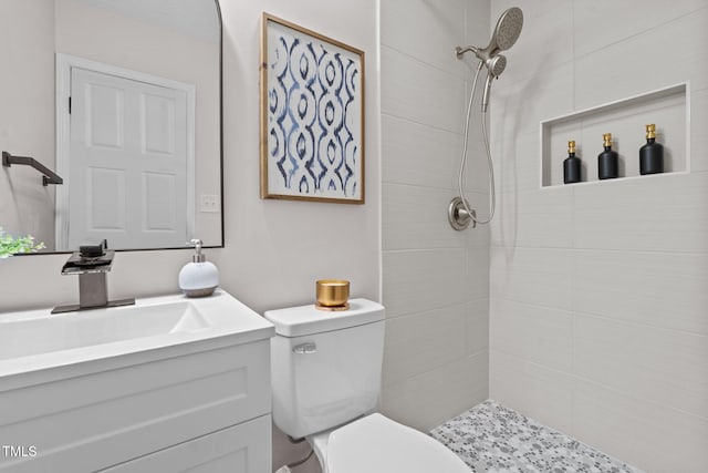 bathroom with a tile shower, toilet, and vanity