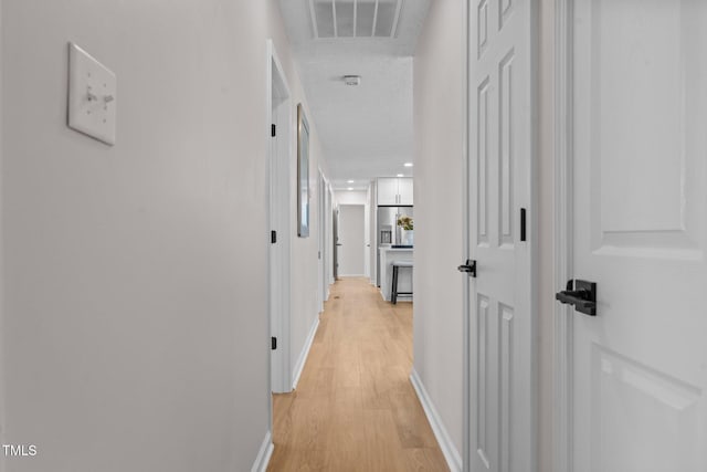 hallway with visible vents, a textured ceiling, baseboards, and light wood-style floors