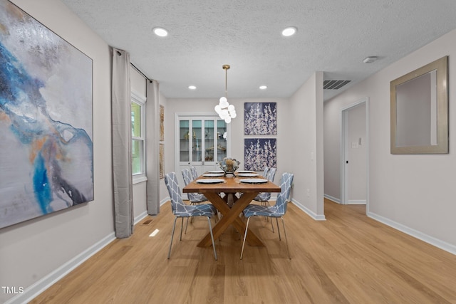 dining space featuring light wood-style flooring, a notable chandelier, baseboards, and visible vents