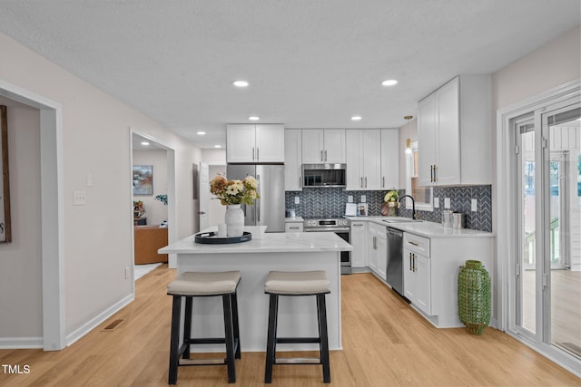 kitchen featuring white cabinetry, a kitchen island, a sink, appliances with stainless steel finishes, and a kitchen bar