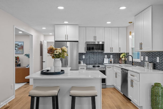 kitchen with a breakfast bar area, light wood-style flooring, a sink, stainless steel appliances, and white cabinets