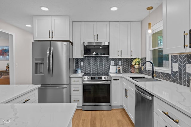 kitchen with light stone counters, light wood-style flooring, appliances with stainless steel finishes, white cabinets, and a sink