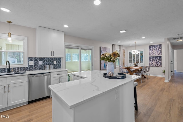 kitchen featuring light wood finished floors, a center island, stainless steel dishwasher, white cabinetry, and a sink