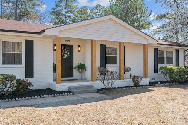 view of front of property featuring crawl space, covered porch, a shingled roof, and brick siding