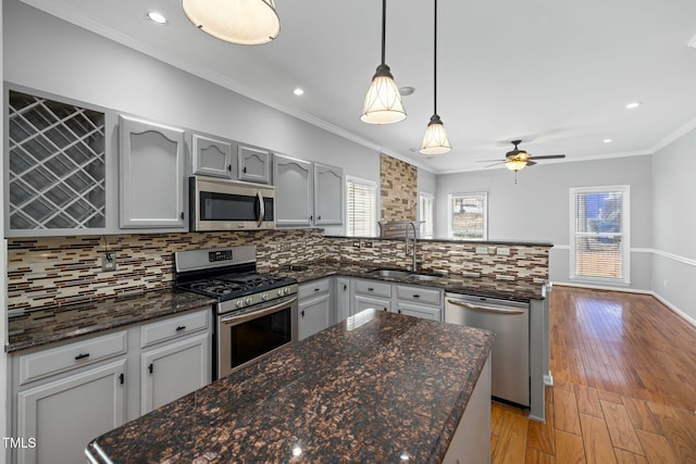 kitchen with a sink, tasteful backsplash, stainless steel appliances, a peninsula, and crown molding