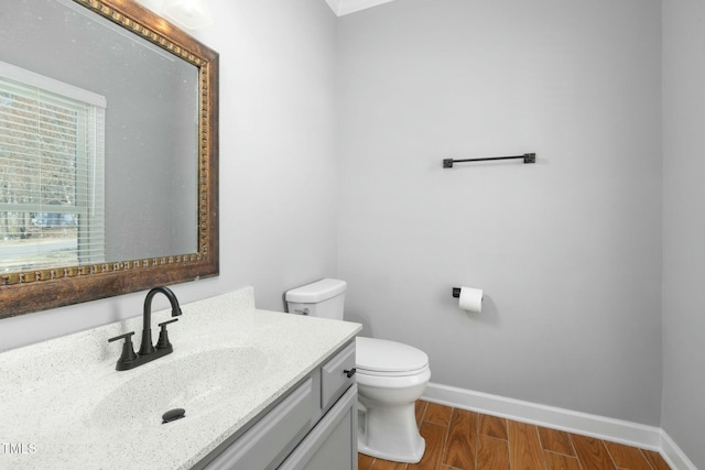 bathroom with vanity, toilet, wood finished floors, and baseboards