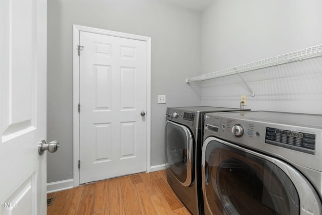 washroom with laundry area, washing machine and dryer, light wood-type flooring, and baseboards