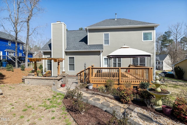 back of property with a wooden deck, roof with shingles, a gazebo, a chimney, and a pergola