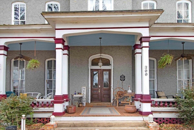 doorway to property with a ceiling fan, covered porch, french doors, and stucco siding