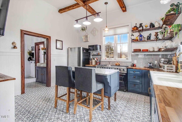 kitchen with blue cabinets, beamed ceiling, appliances with stainless steel finishes, and wood counters