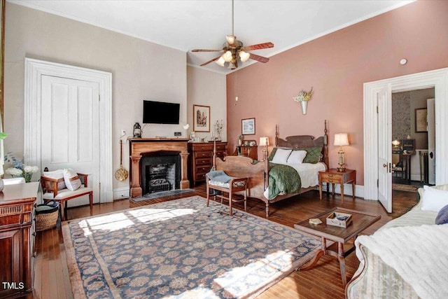 bedroom featuring a fireplace with flush hearth, ornamental molding, wood finished floors, baseboards, and ceiling fan