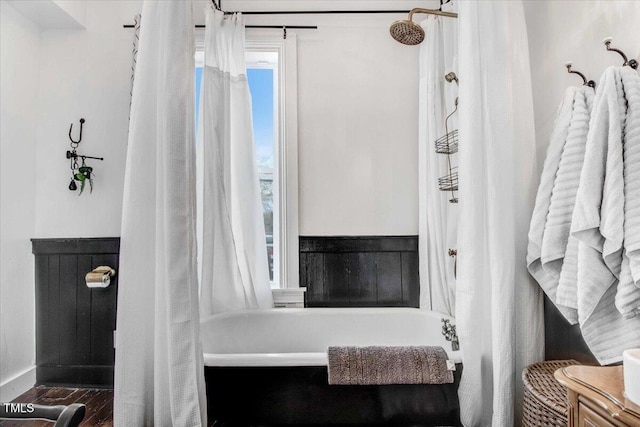 full bathroom with wood finished floors, a tub to relax in, and baseboards