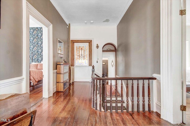 hallway with an upstairs landing, wood finished floors, and ornamental molding