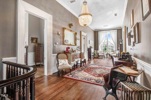 interior space with an inviting chandelier, crown molding, wood finished floors, and a wainscoted wall