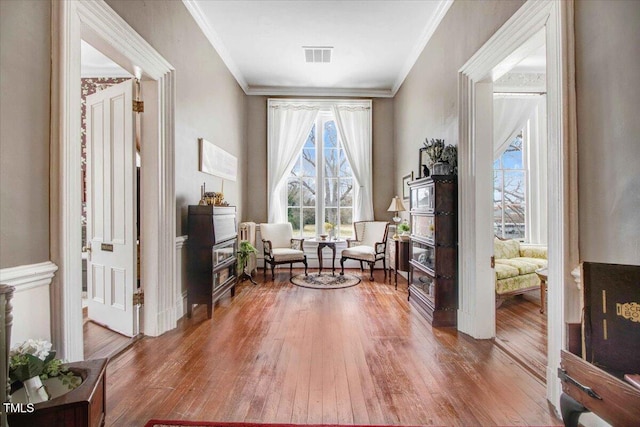 living area with crown molding, wood finished floors, and visible vents